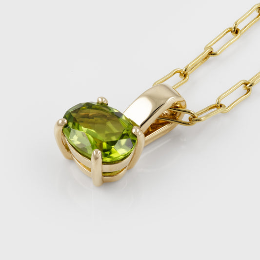 A yellow gold pendant necklace featuring a large, oval-cut green peridot gemstone in a prong setting, suspended from a paperclip chain on a clean white background.