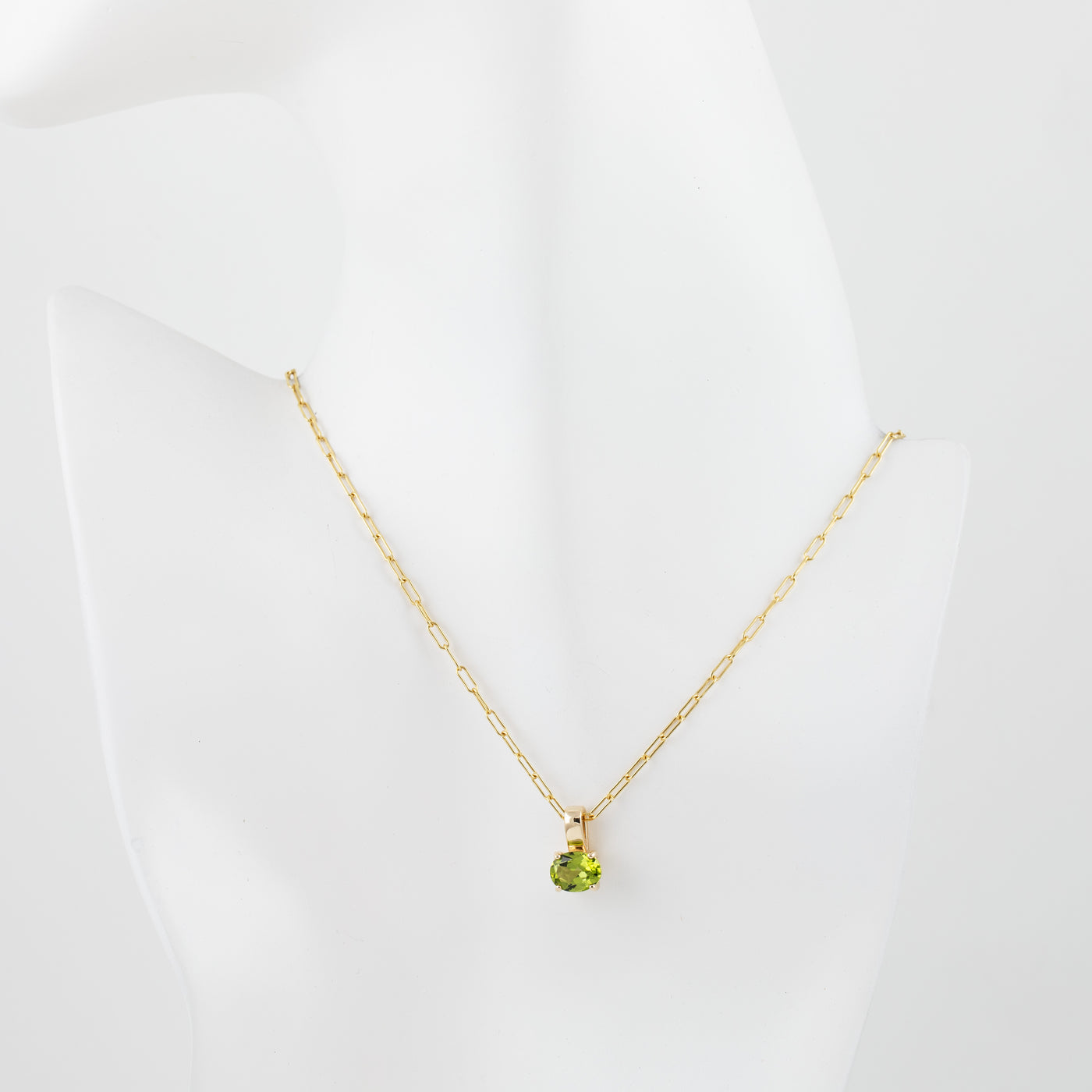 A delicate gold chain necklace with a small round green peridot gemstone pendant, displayed on a white mannequin bust against a clean white background.