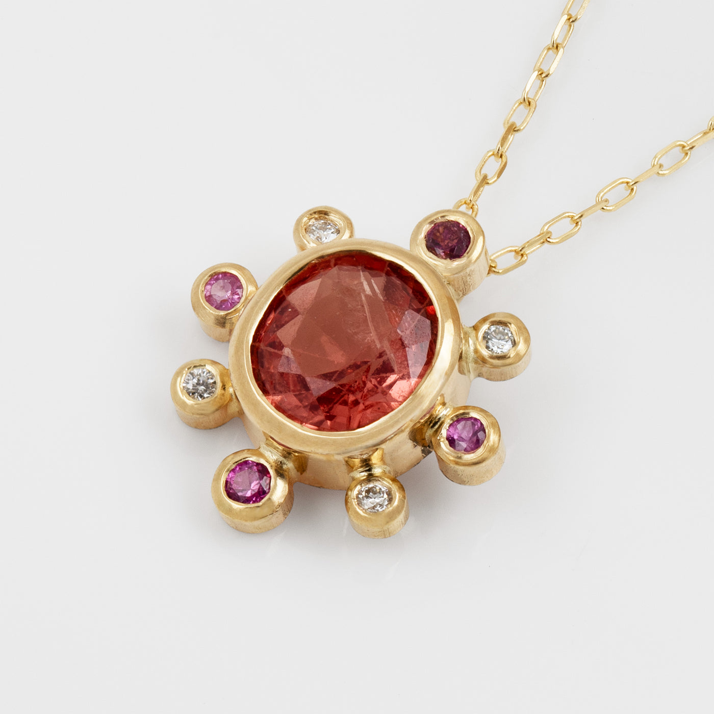 Side view of yellow gold pendant featuring faceted oval orange pink Spinel with pink Sapphire and white Diamond accents
