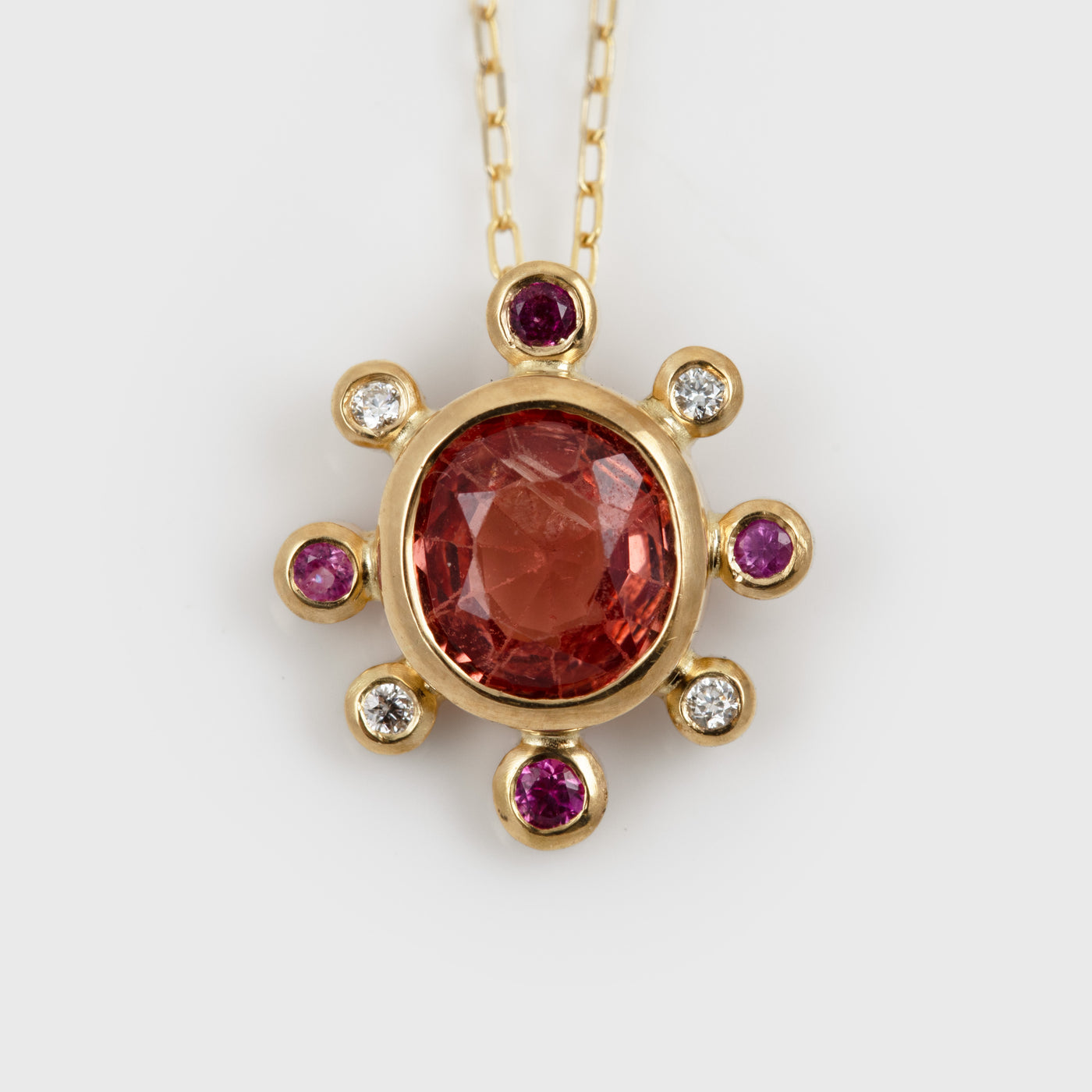 Yellow gold pendant featuring faceted oval orange pink Spinel with pink Sapphire and white Diamond accents
