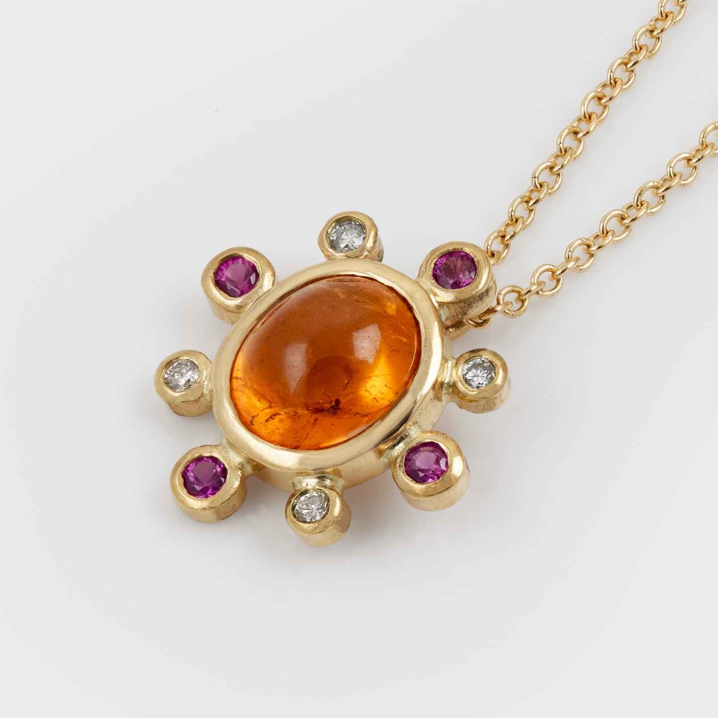 Angled view of yellow gold necklace featuring orange Garnet, pink Sapphires, and white Diamonds