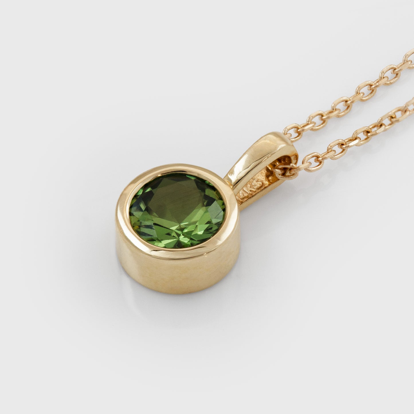 Yellow gold pendant featuring bezel set round green Sapphire suspended from cable chain