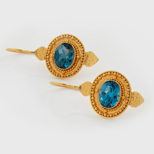 Yellow gold earrings featuring oval blue topaz center stones in center, accented by gold wire and textured details, photographed on a white background
