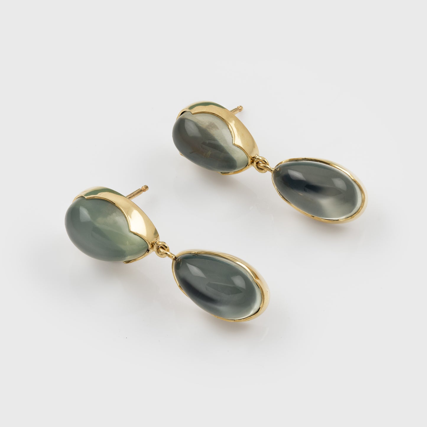 A pair of gold drop earrings with oval green-gray cabochon gemstones, shown on a clean light gray background.