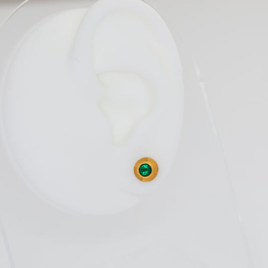Close-up of a white ear mannequin with a green gemstone stud earring on a light gray background