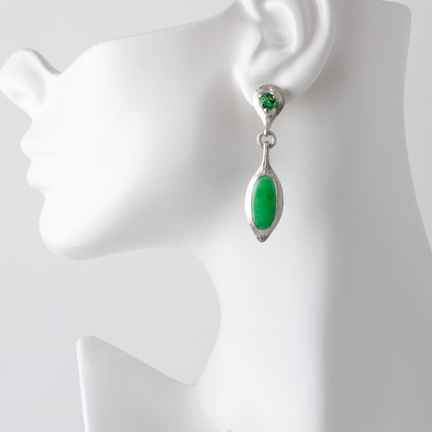 Green teardrop earring on a white mannequin ear