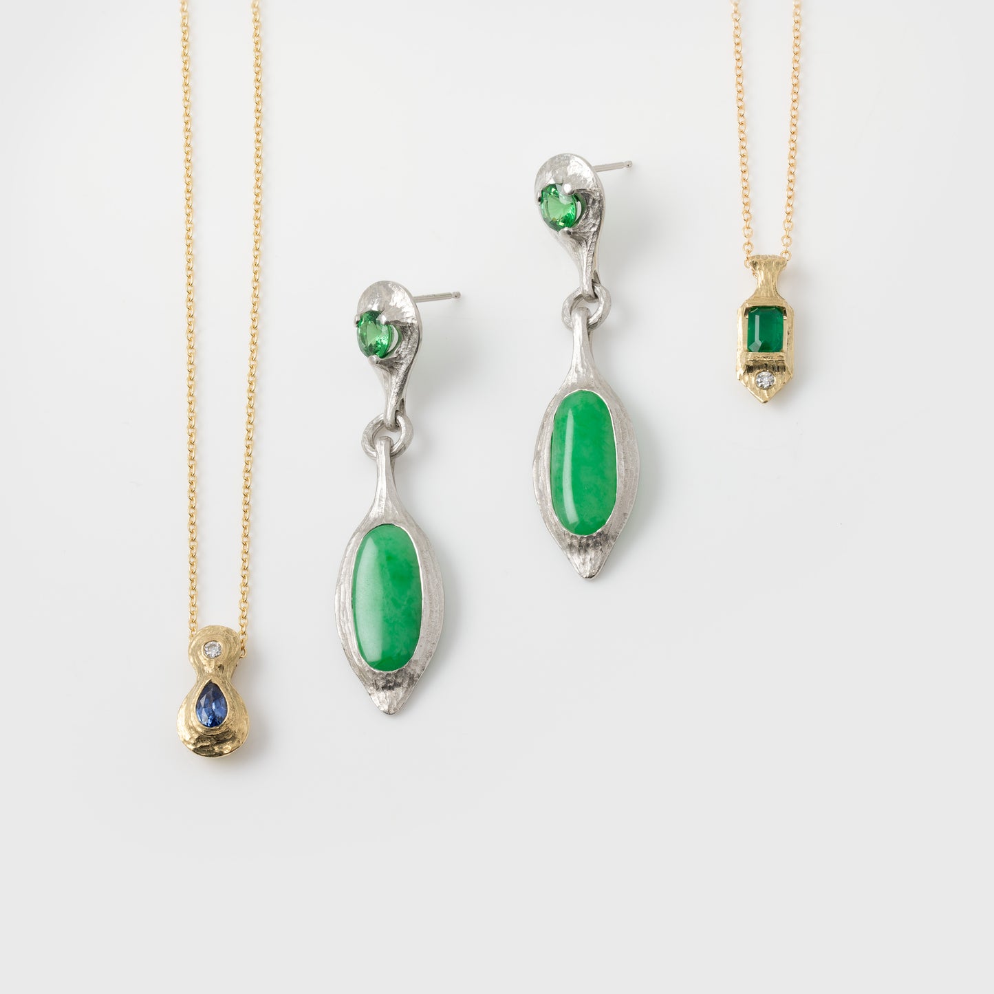 Jewelry set with green gemstones on gold and silver chains against a white background