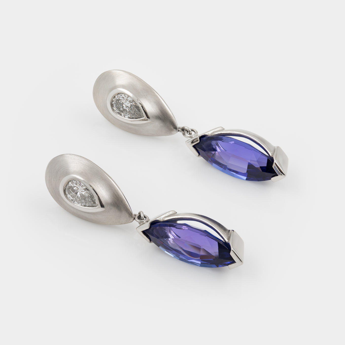 Pair of platinum earrings with tanzanite gemstones on a white background