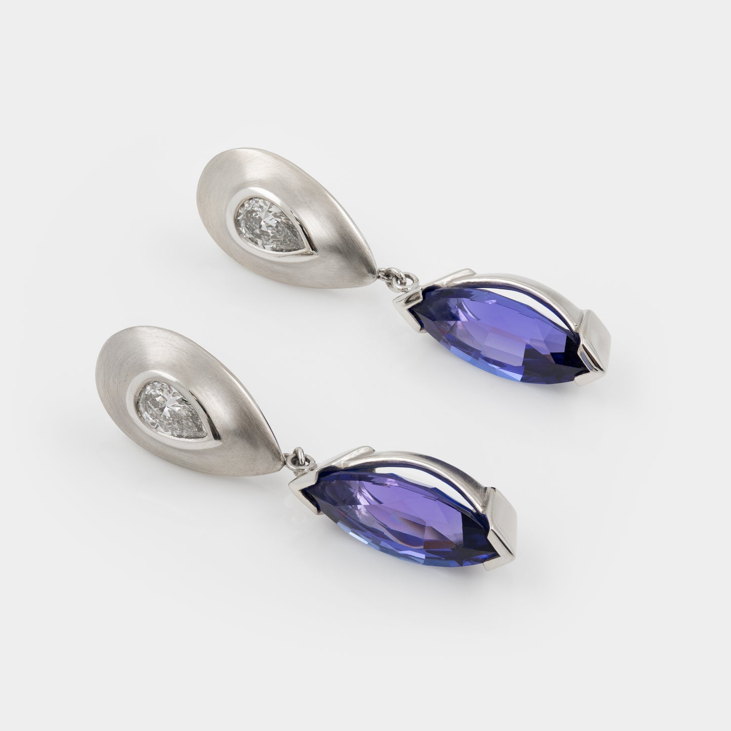 Pair of platinum earrings with tanzanite gemstones on a white background