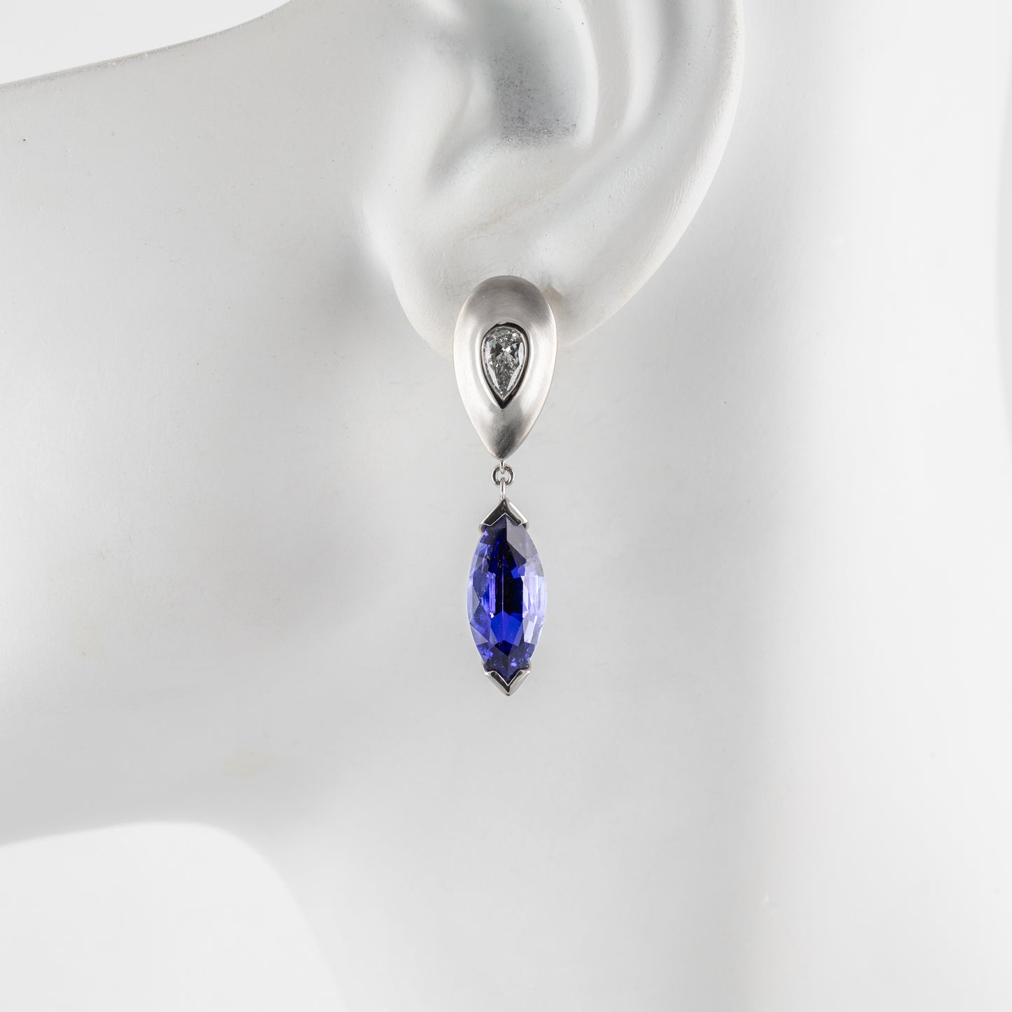 Platinum earring with a tanzanite gemstone on a mannequin ear.