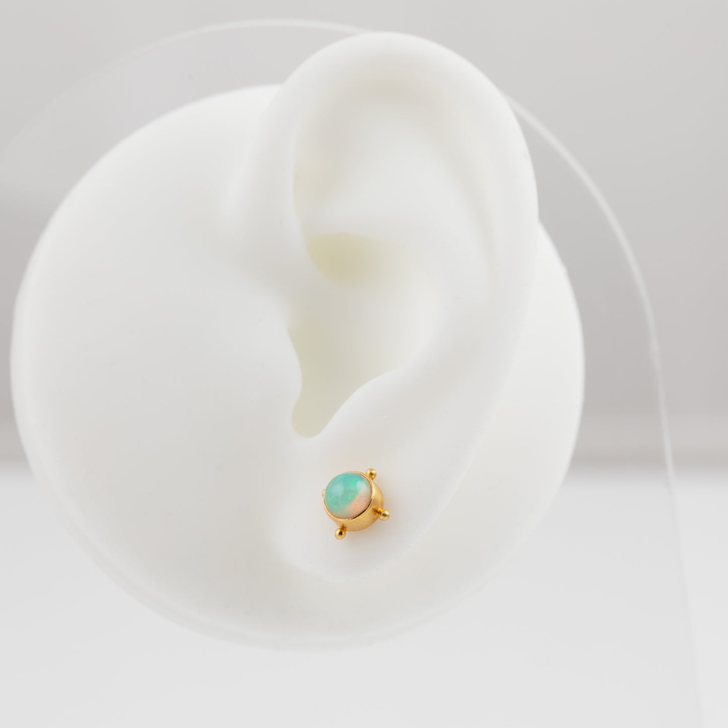 Gold earring with opal on a white mannequin ear 