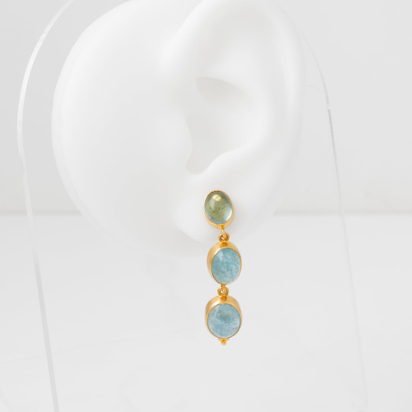 Pair of earrings with gold frames and aquamarine gemstones on a white mannequin