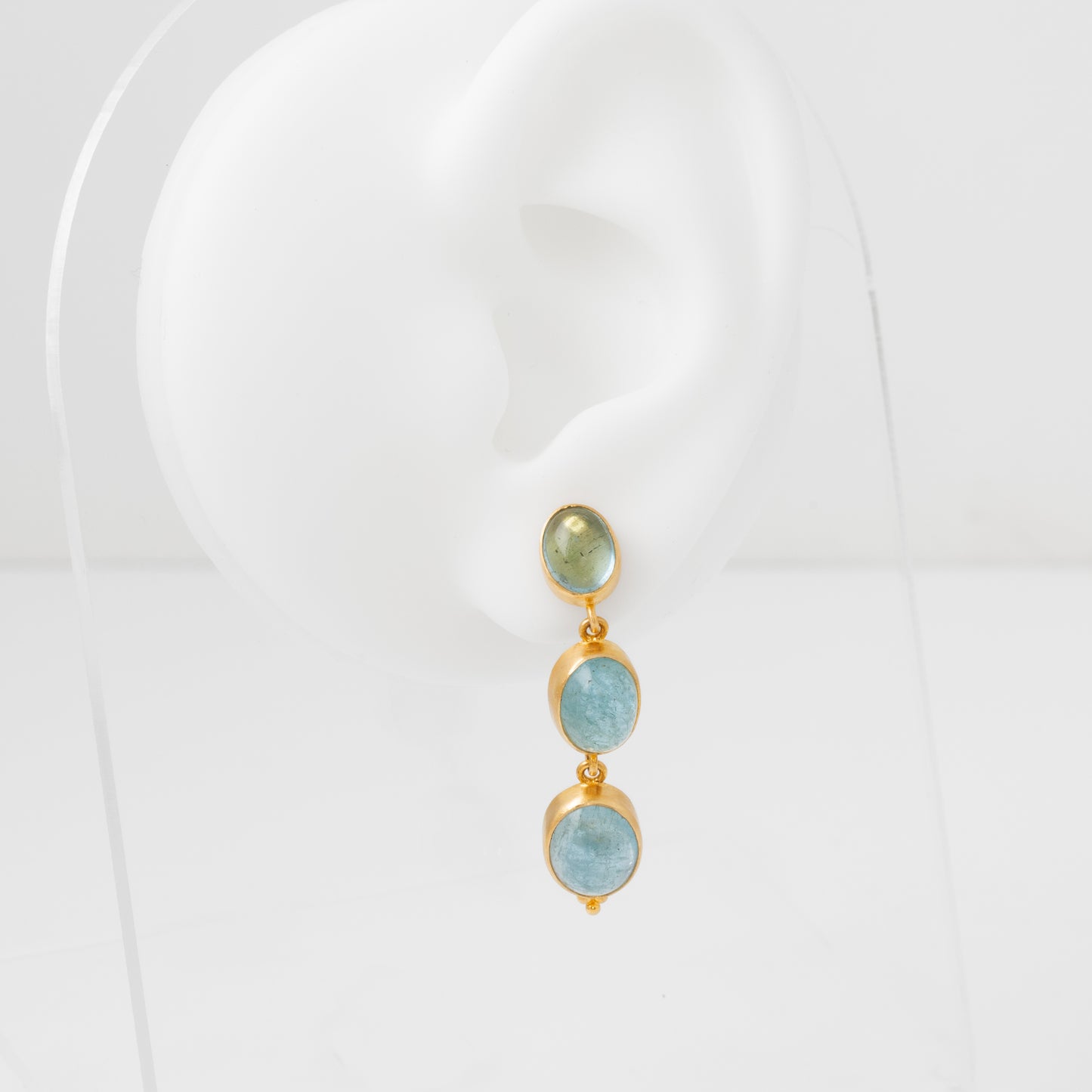 Pair of earrings with gold frames and aquamarine gemstones on a white mannequin