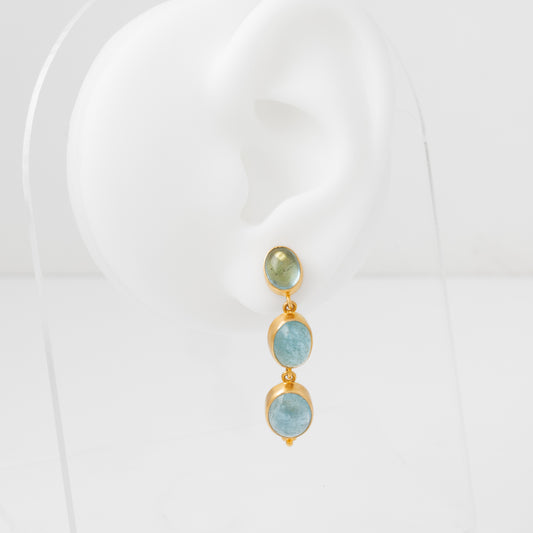 Pair of earrings with gold frames and aquamarine gemstones on a white mannequin