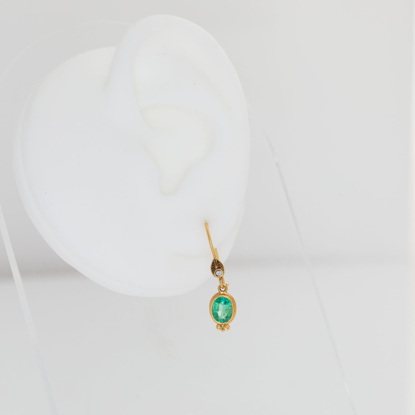 Gold earring with a green gemstone on a white background