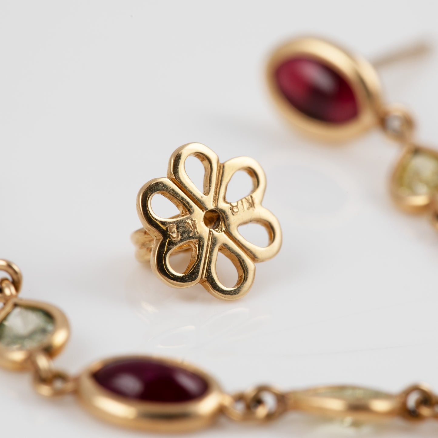 Gold flower-shaped earring backing, shown in close-up on a white background with matching gold earrings partially visible.