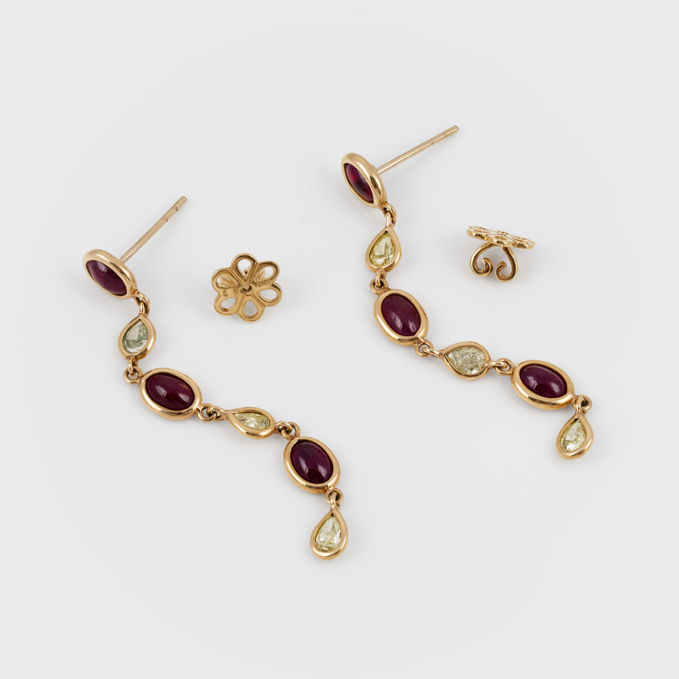 A pair of gold drop earrings with oval dark red gemstones and small diamonds, shown on a light gray background with matching flower-shaped earring backings.