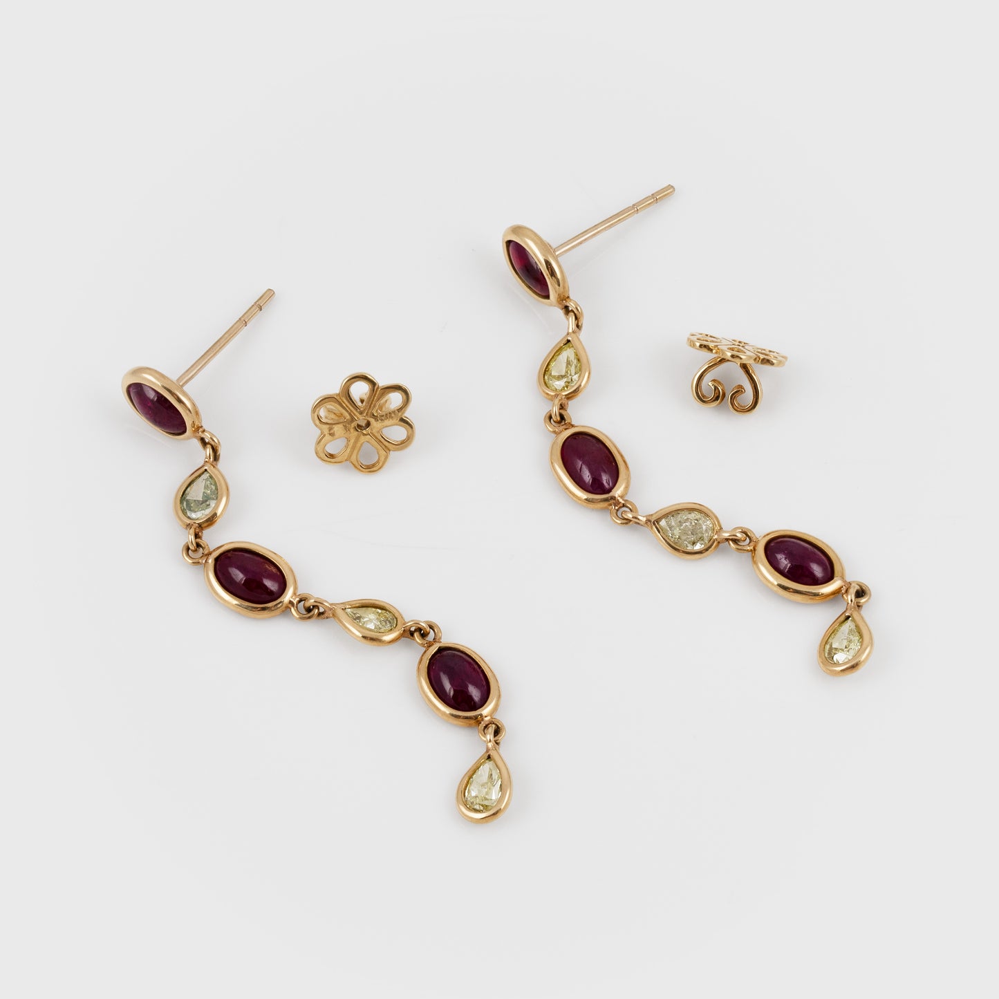 A pair of gold drop earrings with oval dark red gemstones and small diamonds, shown on a light gray background with matching flower-shaped earring backings.
