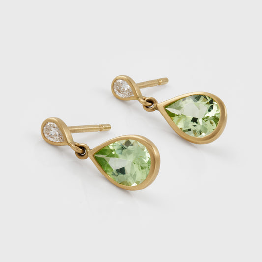 A pair of gold drop earrings featuring faceted light green teardrop-shaped gemstones and a small diamond at the top of each earring, shown on a light gray background.