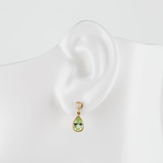 A gold drop earring with a light green teardrop gemstone and a small diamond accent stone, displayed on a white mannequin ear.