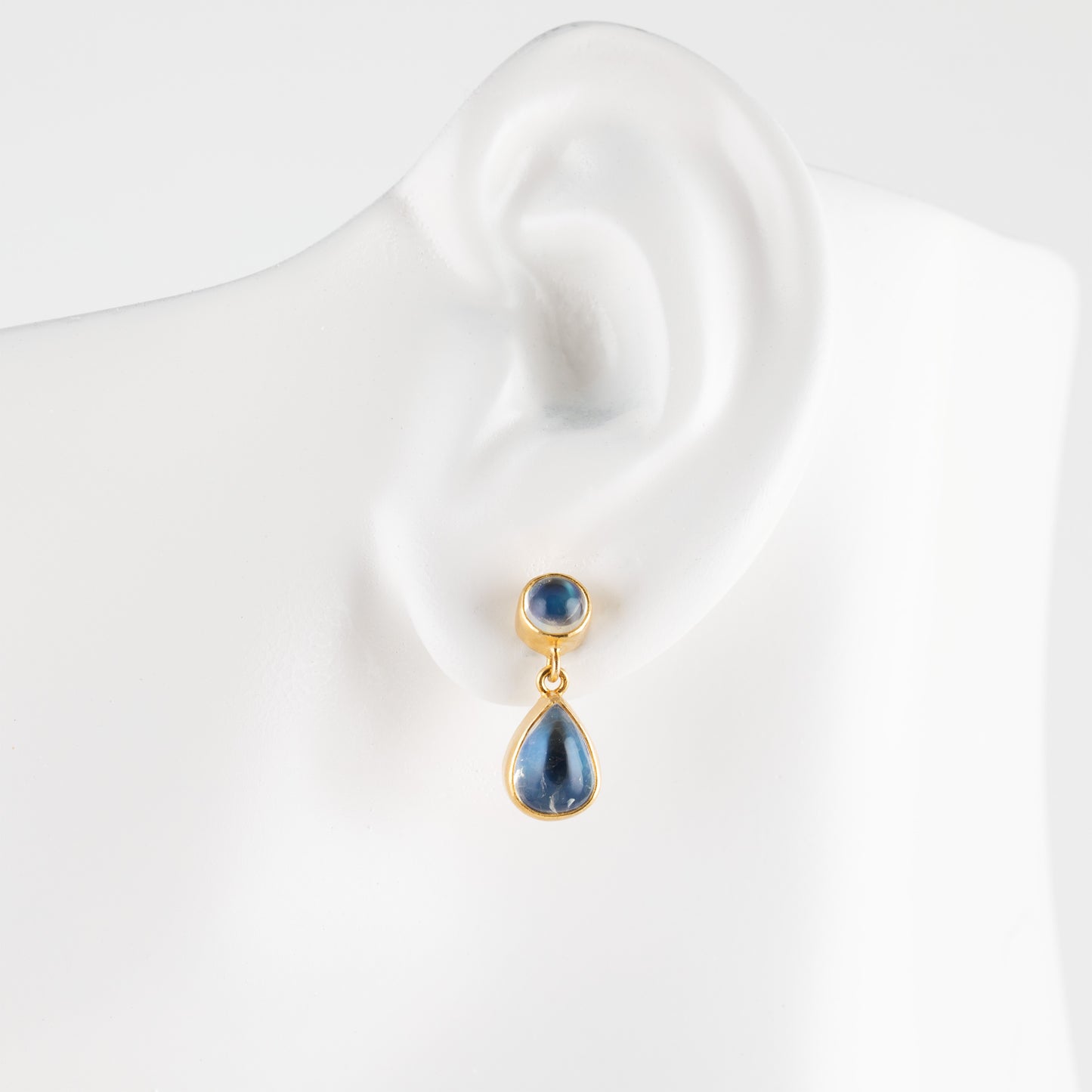A gold teardrop stud earring, displayed on a white ear-shaped mannequin bust.