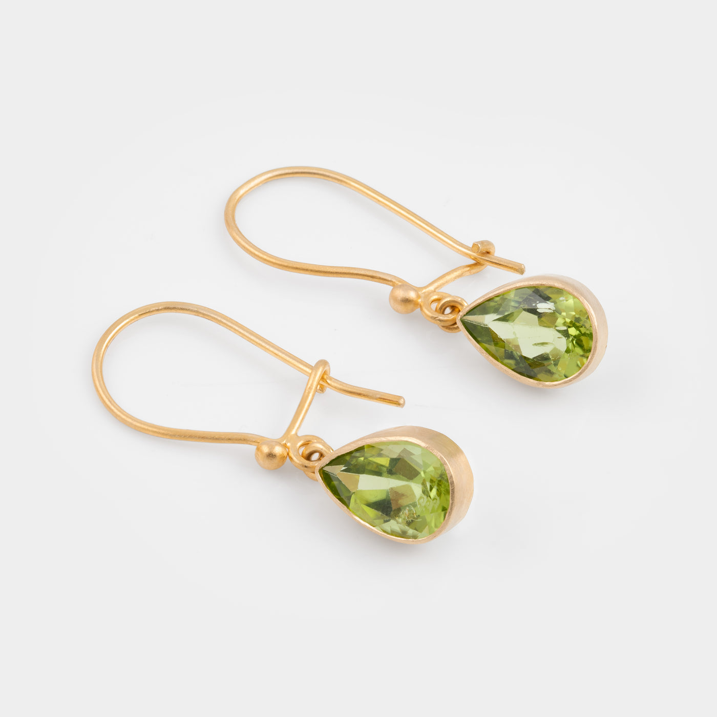 A pair of gold drop earrings with faceted green gemstones, displayed on a clean light gray background.