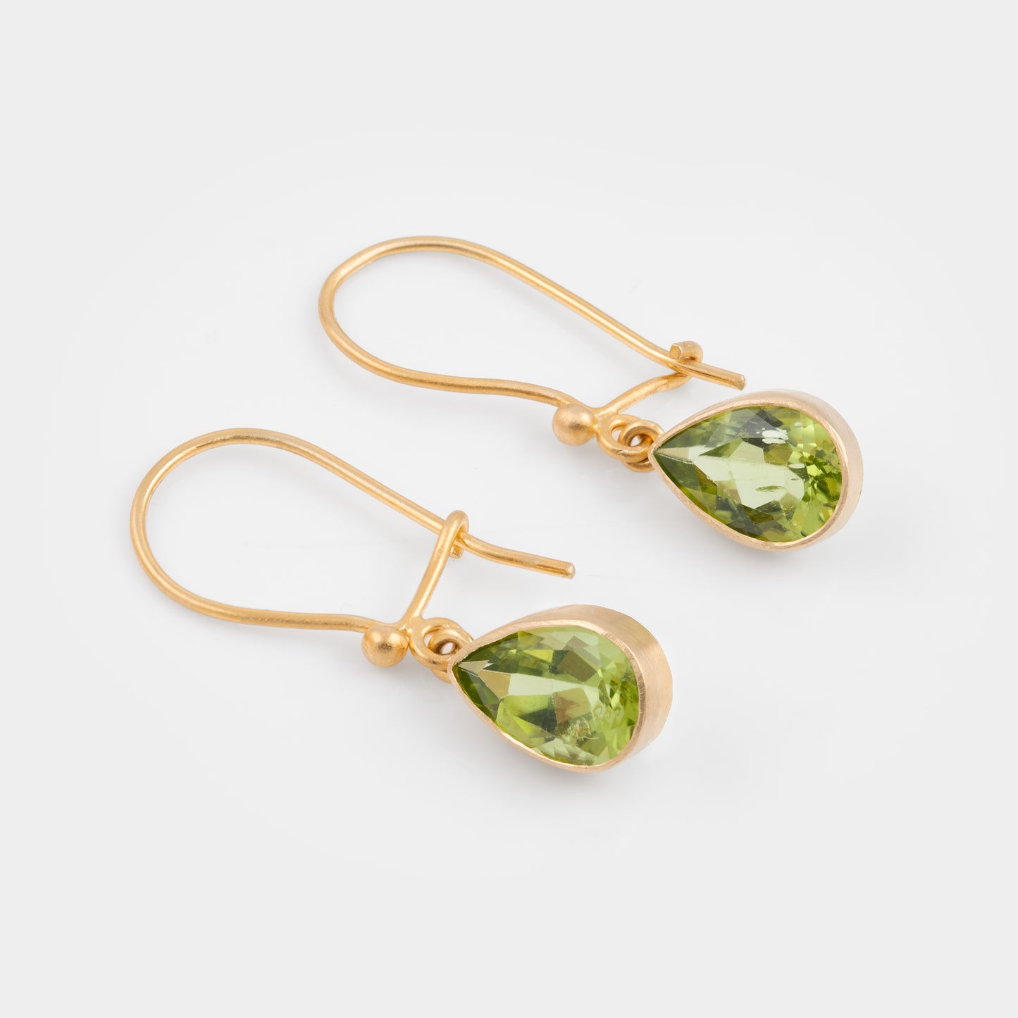 A pair of gold drop earrings with faceted green gemstones, displayed on a clean light gray background.