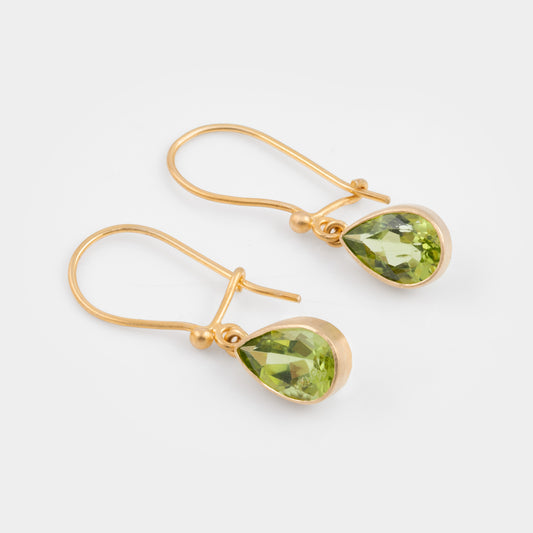 A pair of gold drop earrings with faceted green gemstones, displayed on a clean light gray background.