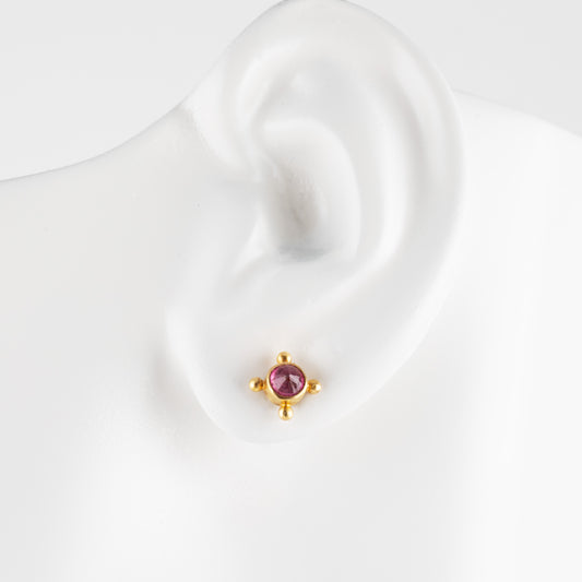 A small gold stud earring with a round gemstone, displayed on a white ear-shaped mannequin stand against a white background.