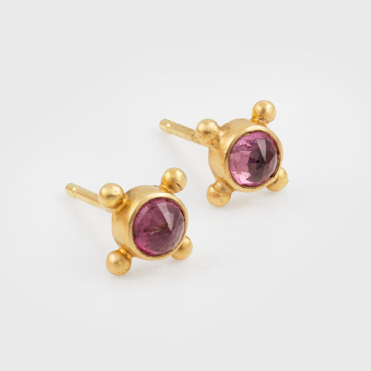 A pair of gold stud earrings with round faceted pink gemstones and small gold bead accents, shown on a clean white background.