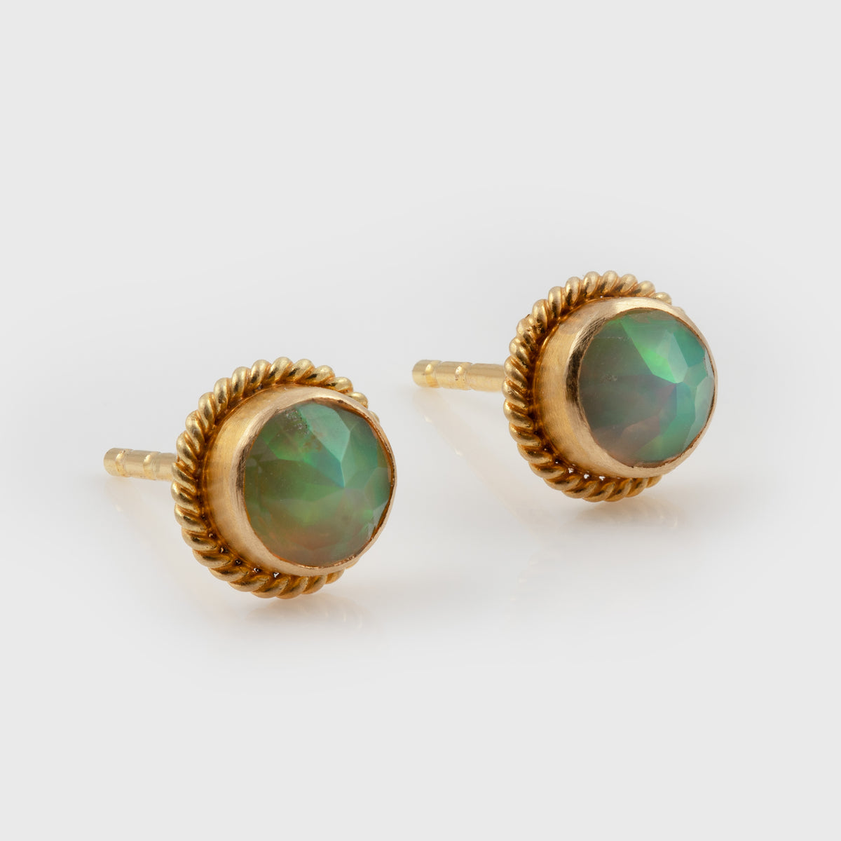 A pair of gold stud earrings with round iridescent green opal centers and twisted rope-style gold borders, photographed on a white background.