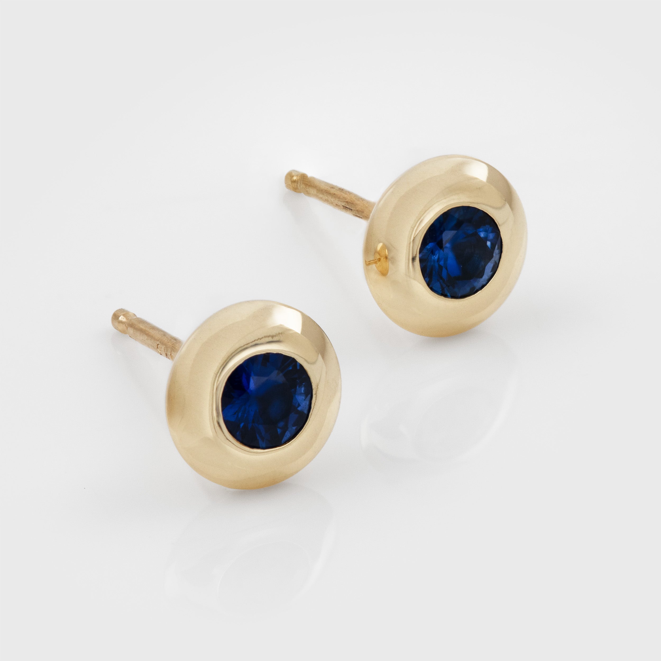 Yellow gold stud earrings featuring bezel set blue Sapphires