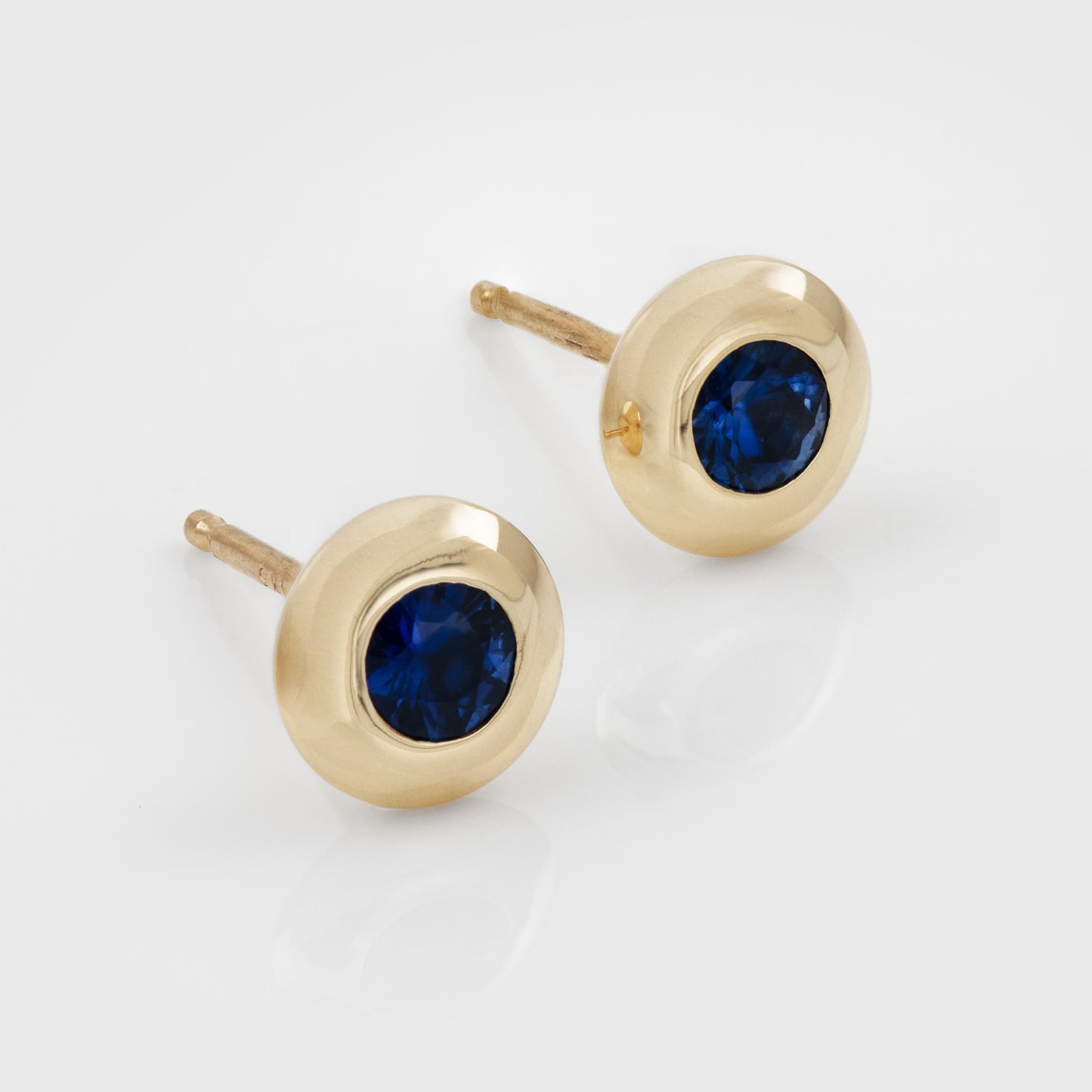 Yellow gold stud earrings featuring bezel set blue Sapphires