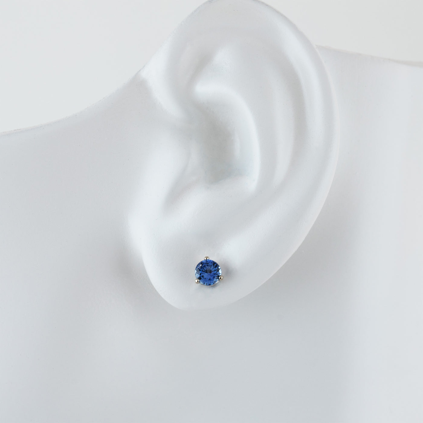 Single white gold stud earring featuring round blue Sapphire on white ear model