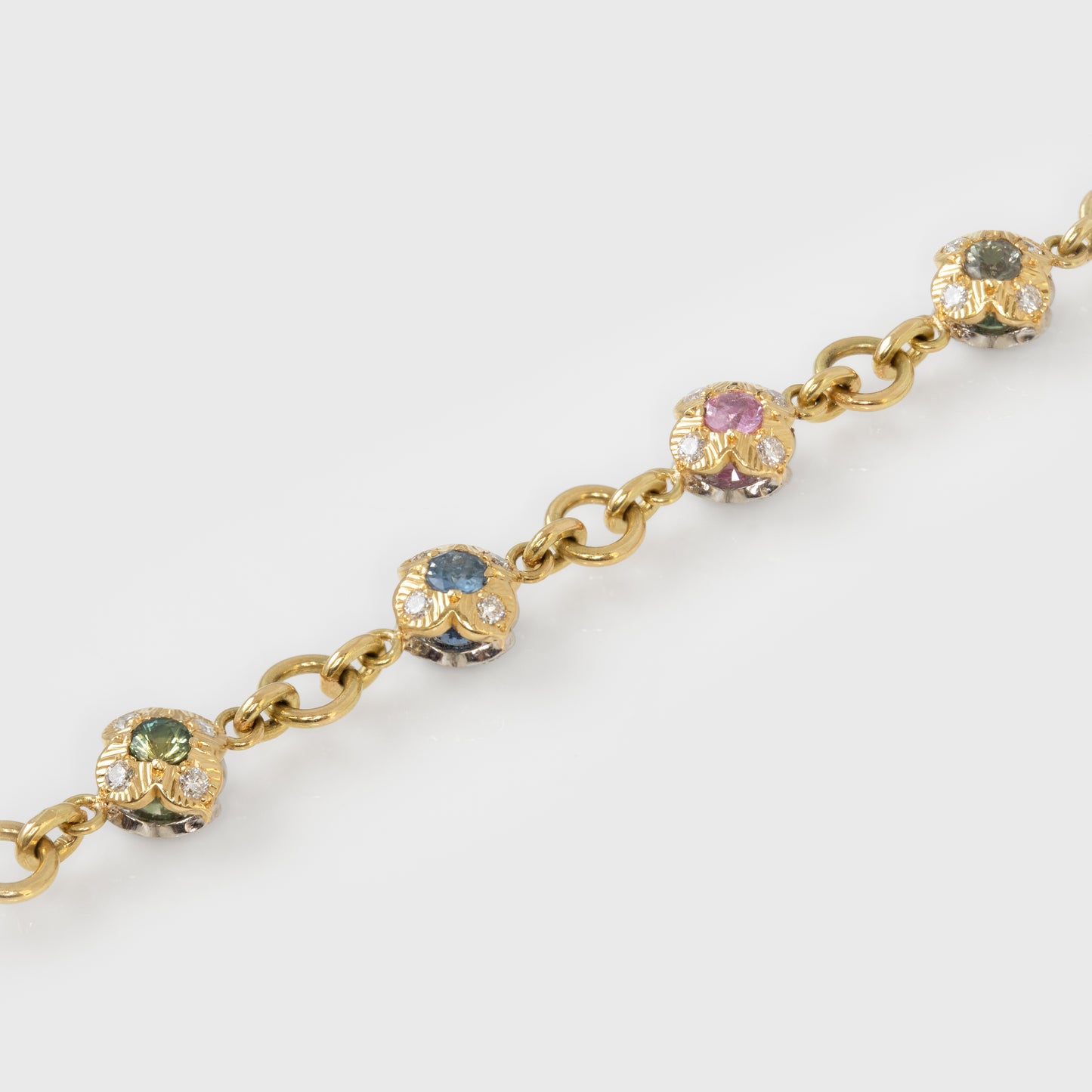 Gold bracelet with colorful gemstones in flower shapes on a white background