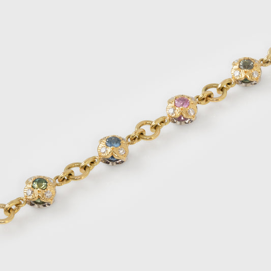 Gold bracelet with colorful gemstones in flower shapes on a white background