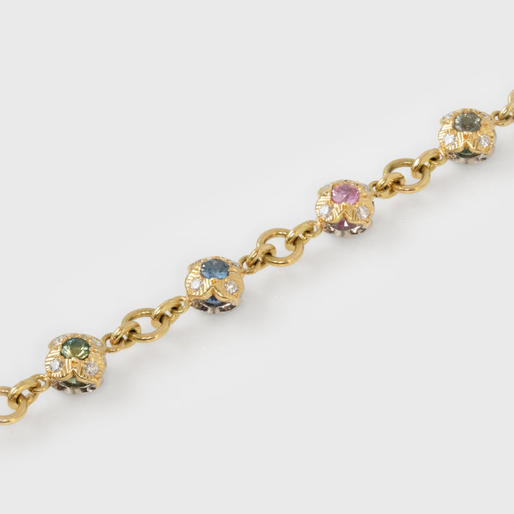 Gold bracelet with colorful gemstones in flower shapes on a white background