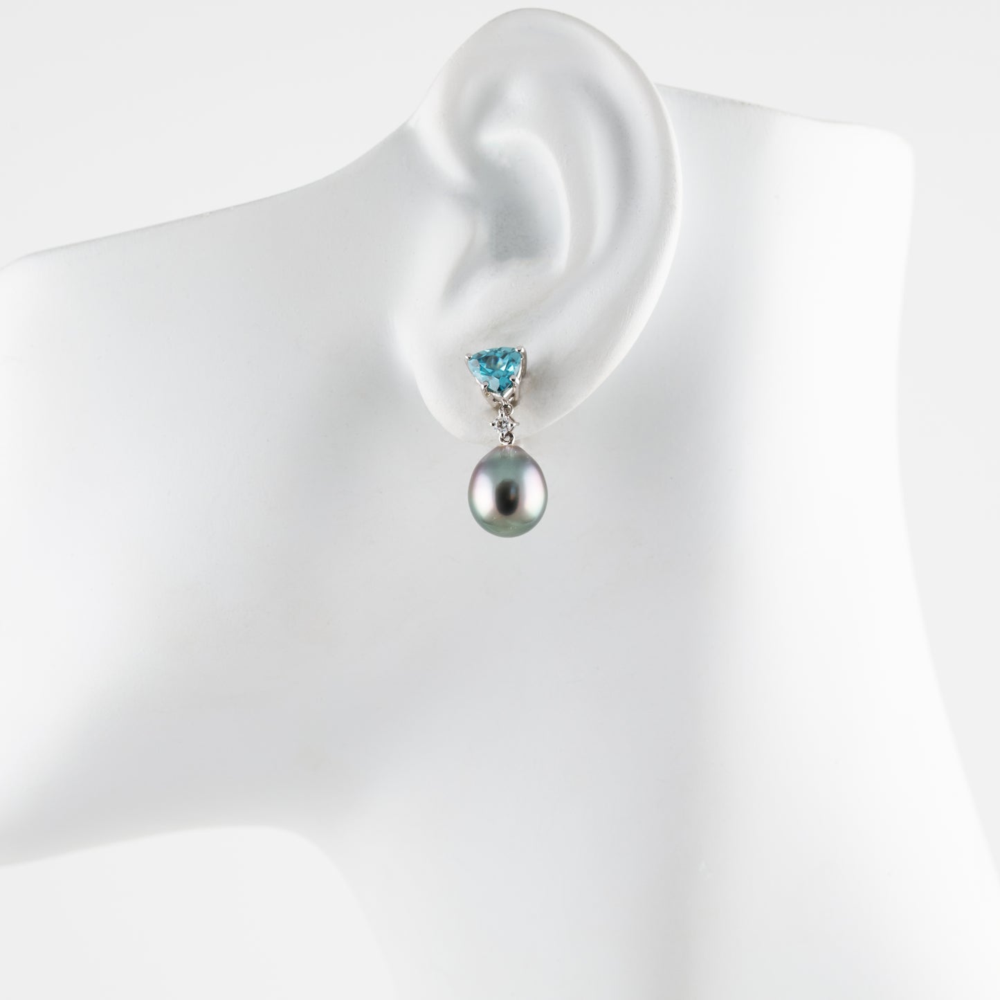 Pearl earring with a blue gemstone on a mannequin ear against a white background