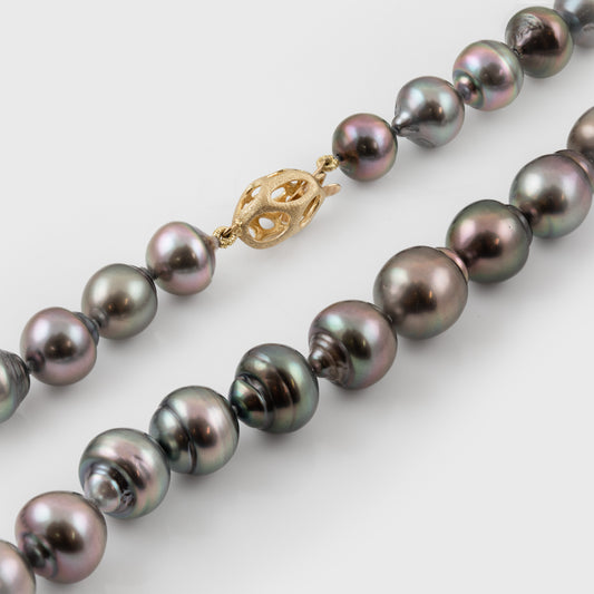 Strand of blue/purplish Tahitian pearls with a gold clasp on a white background