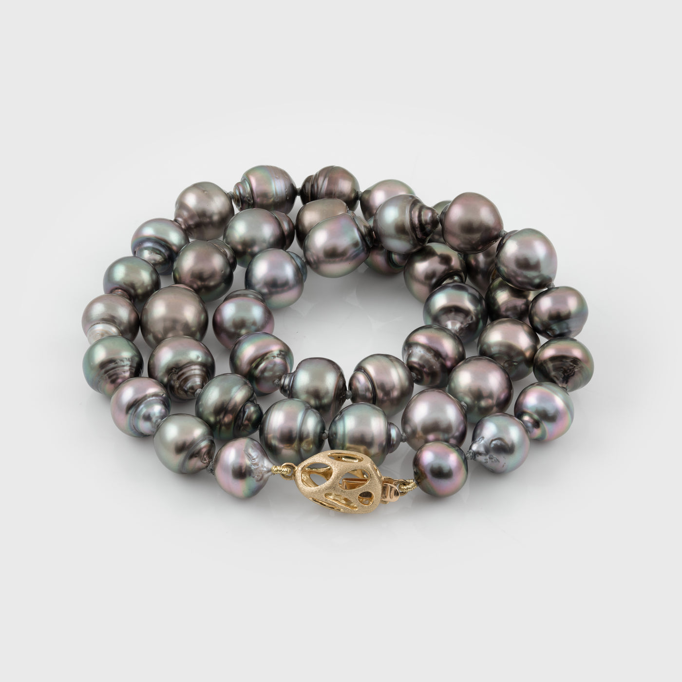 Strand of blue/purplish Tahitian pearls with a gold clasp on a white background