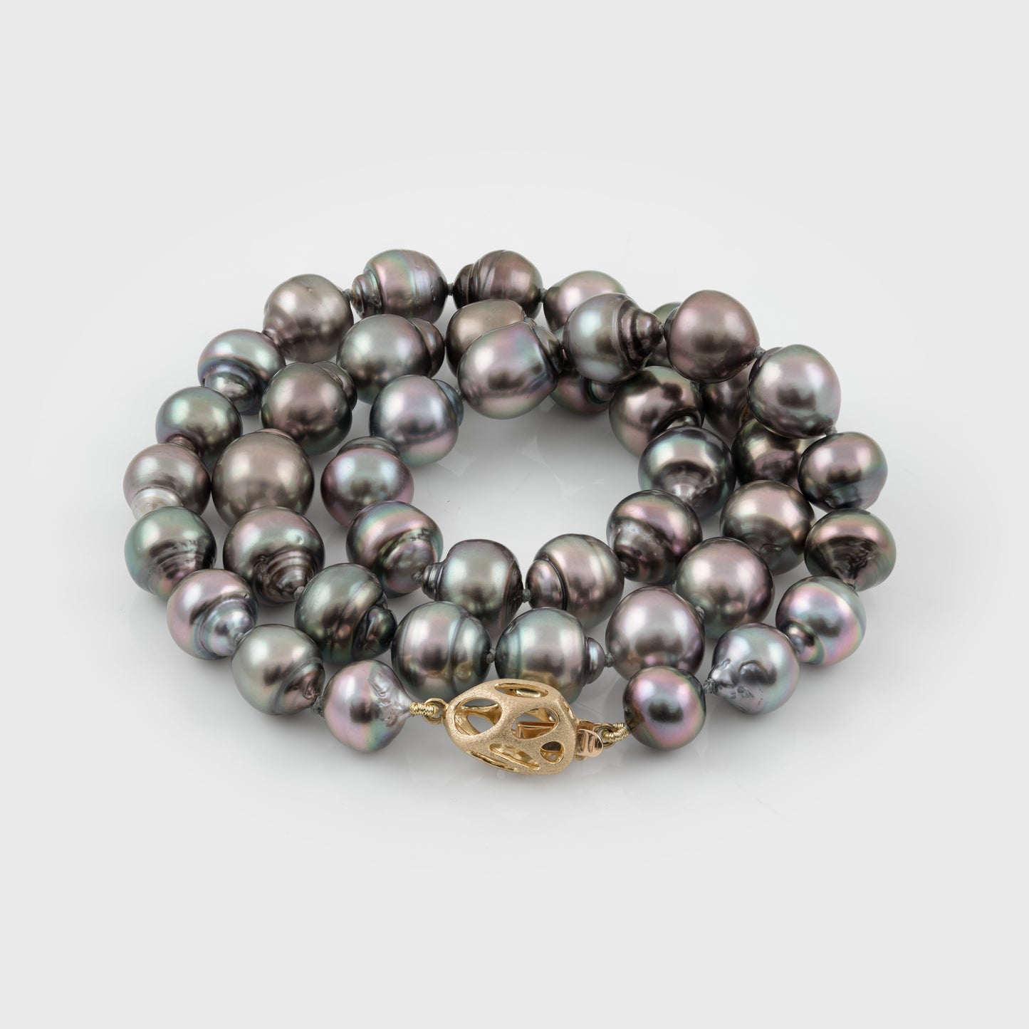 Strand of blue/purplish Tahitian pearls with a gold clasp on a white background