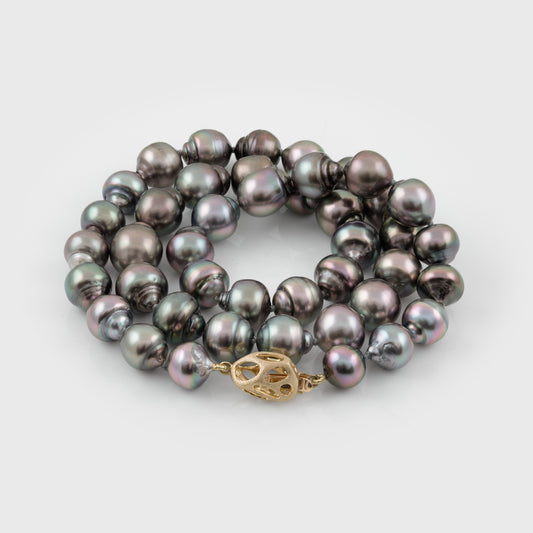 Strand of blue/purplish Tahitian pearls with a gold clasp on a white background