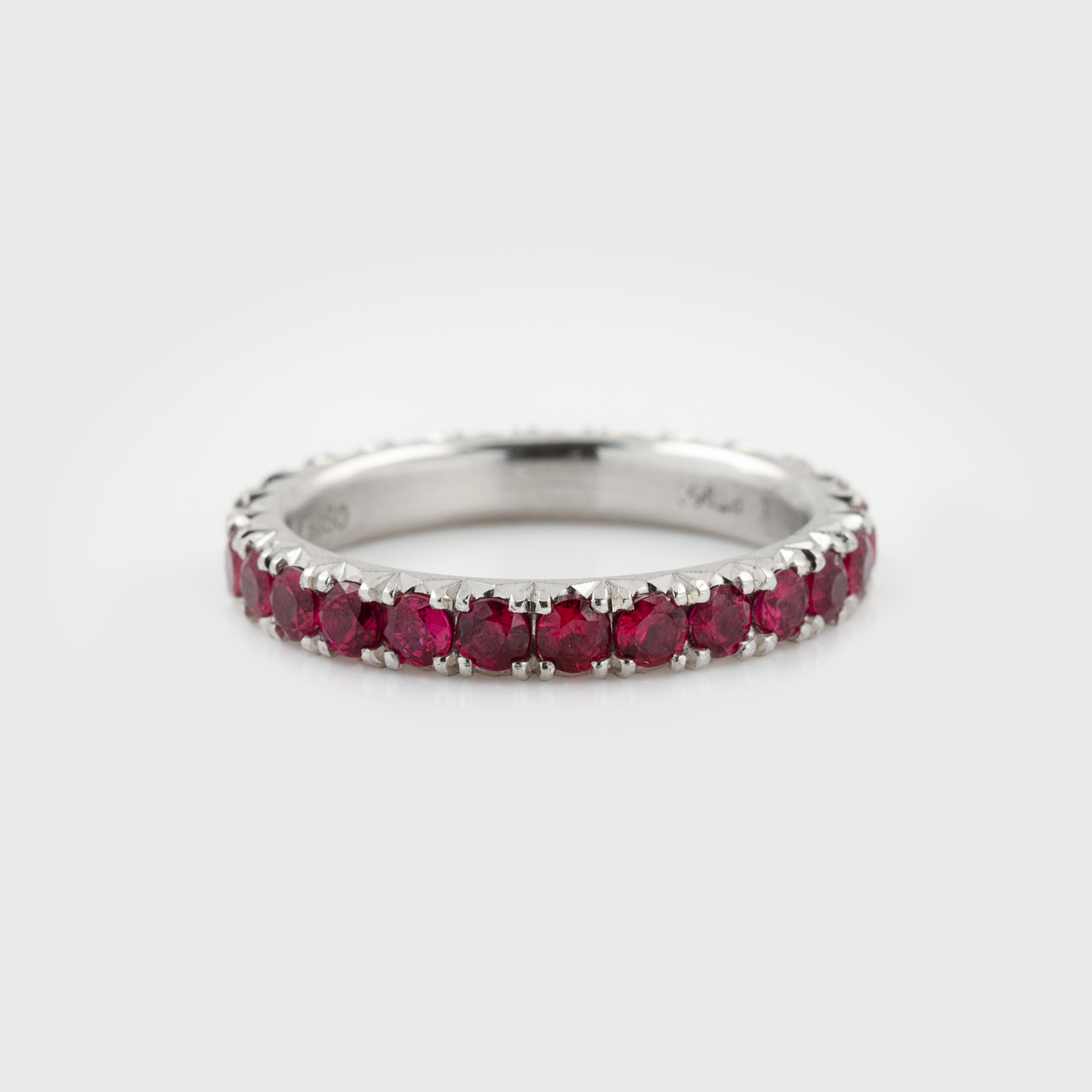 Platinum ring featuring faceted round rubies in an eternity band design with a satin finish, photographed on a white background.