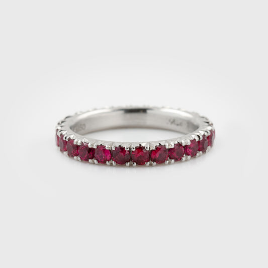 Platinum ring featuring faceted round rubies in an eternity band design with a satin finish, photographed on a white background.