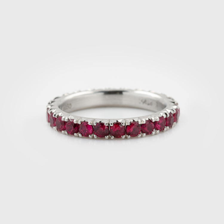 Platinum ring featuring faceted round rubies in an eternity band design with a satin finish, photographed on a white background.