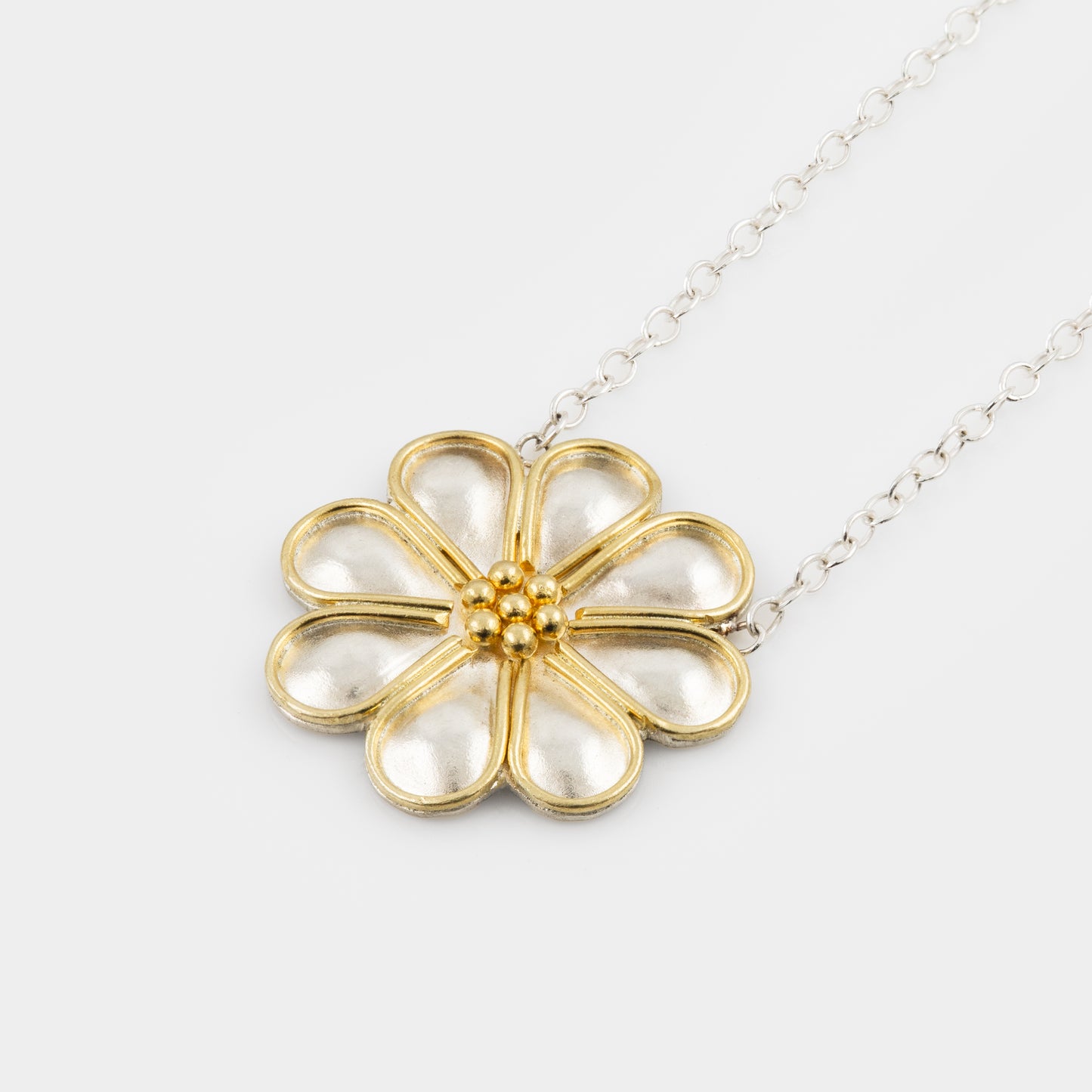 Gold and silver flower-shaped pendant on a silver chain against a white background