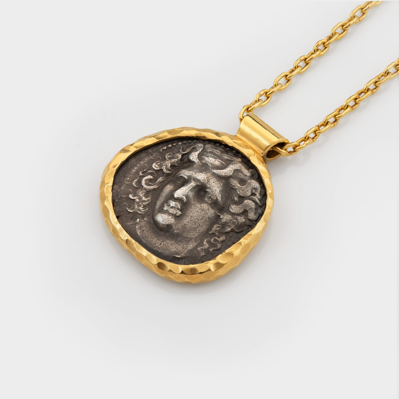 Gold necklace with an ancient coin pendant depicting Apollo on a light gray background