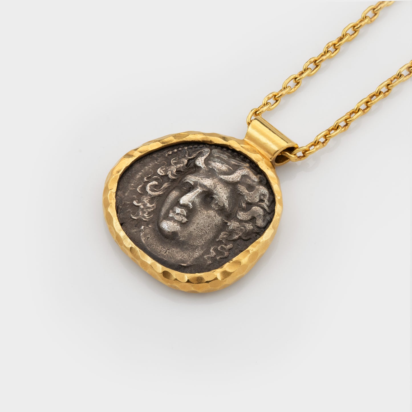 Gold necklace with an ancient coin pendant depicting Apollo on a light gray background