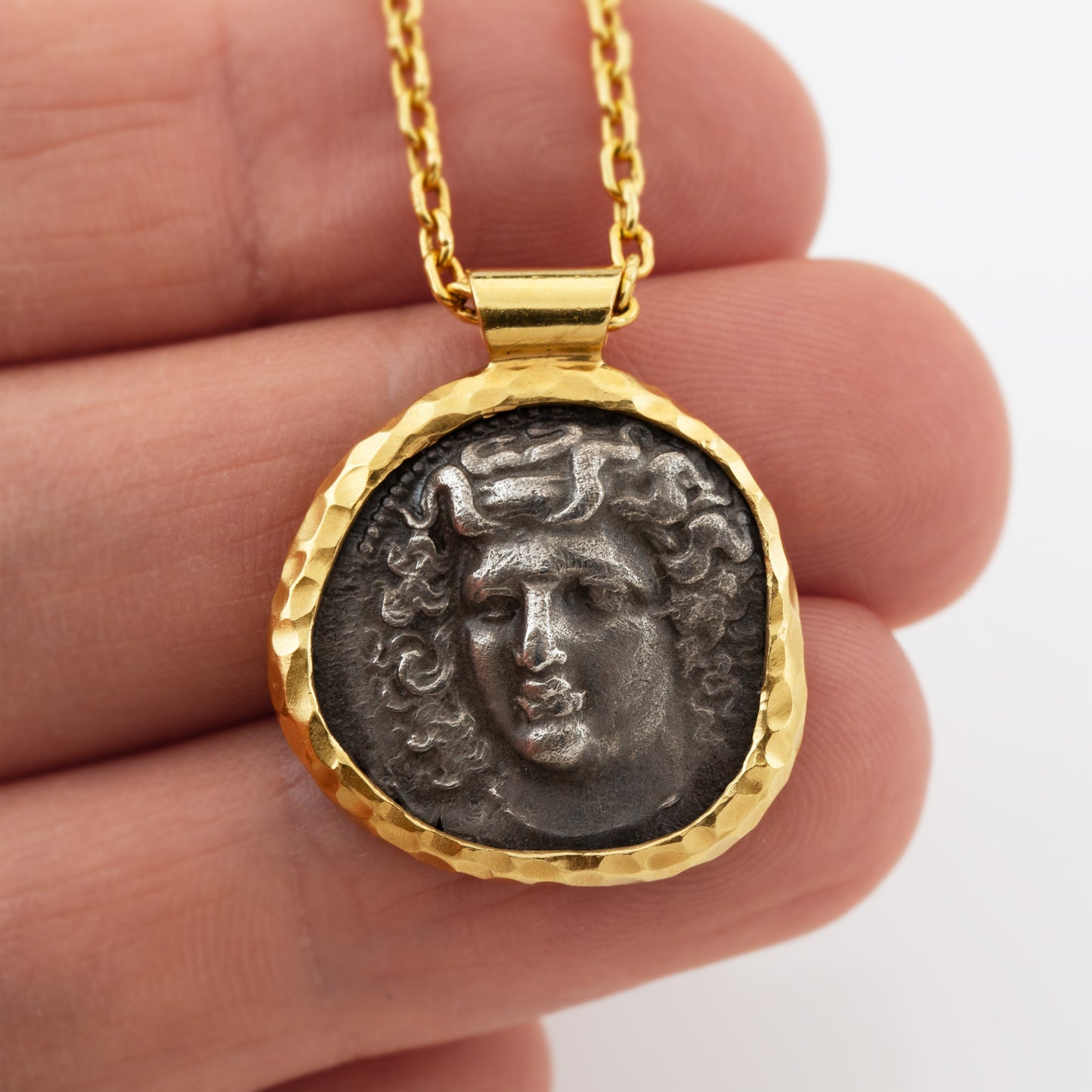 Gold necklace with an ancient coin pendant depicting Apollo on a hand