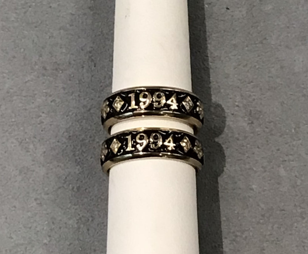 Two bands on a white ring mandrel with a grey background. Rings have the letters 1994 on them. 